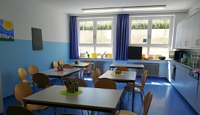 Küchenraum mit Tischen und Stühlen. Blauer Boden mit halbblauer Wand. Küchenzeile zur rechten Seite.nd